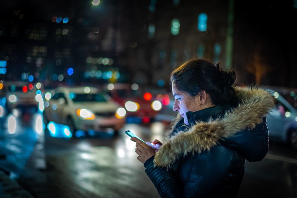 Γυναίκα βράδυ σε κεντρικό δρόμο ψάχνει ταξί από το κινητό της μέσω της πλατφόρμας της Uber 