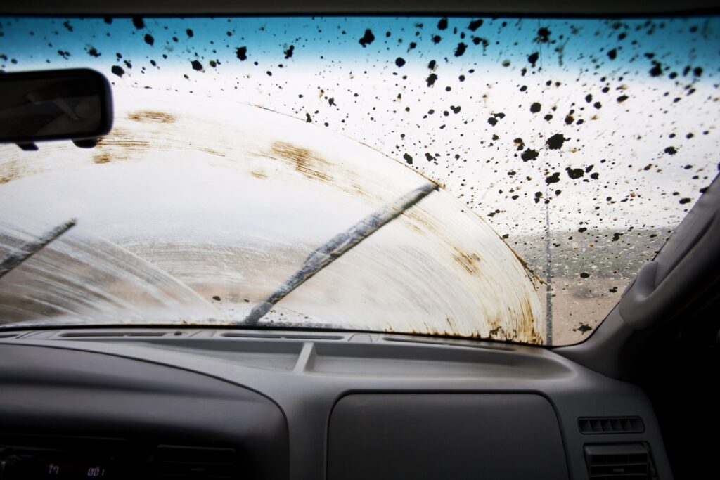 Βρώμικο μπροστινό τζάμι αυτοκινήτου, το οποίο ο οδηγός προσπαθεί να καθαρίσει με τους υαλοκαθαριστήρες